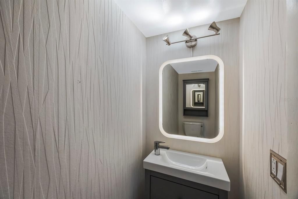 Half bath upstairs for guests has custom wallpaper and mirror for designer touch.