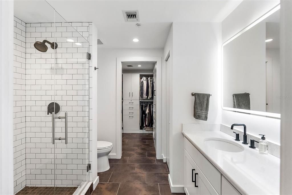 The primary bathroom features a glass-enclosed shower and walk-in closet with a custom buildout