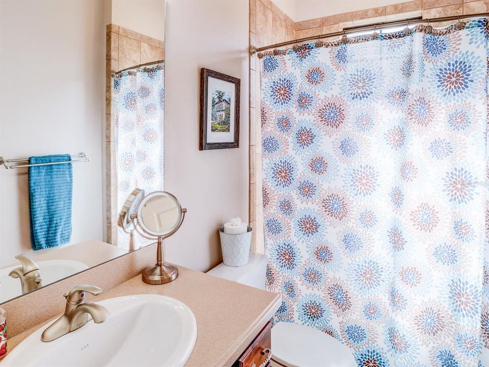 Hall Bath. Tub and shower. Hard surface countertop and wooden cabinet.