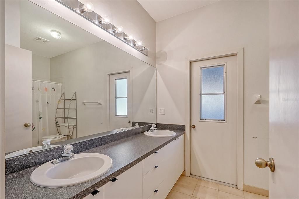 Bathroom 2 with dual vanity & door to lanai/pool