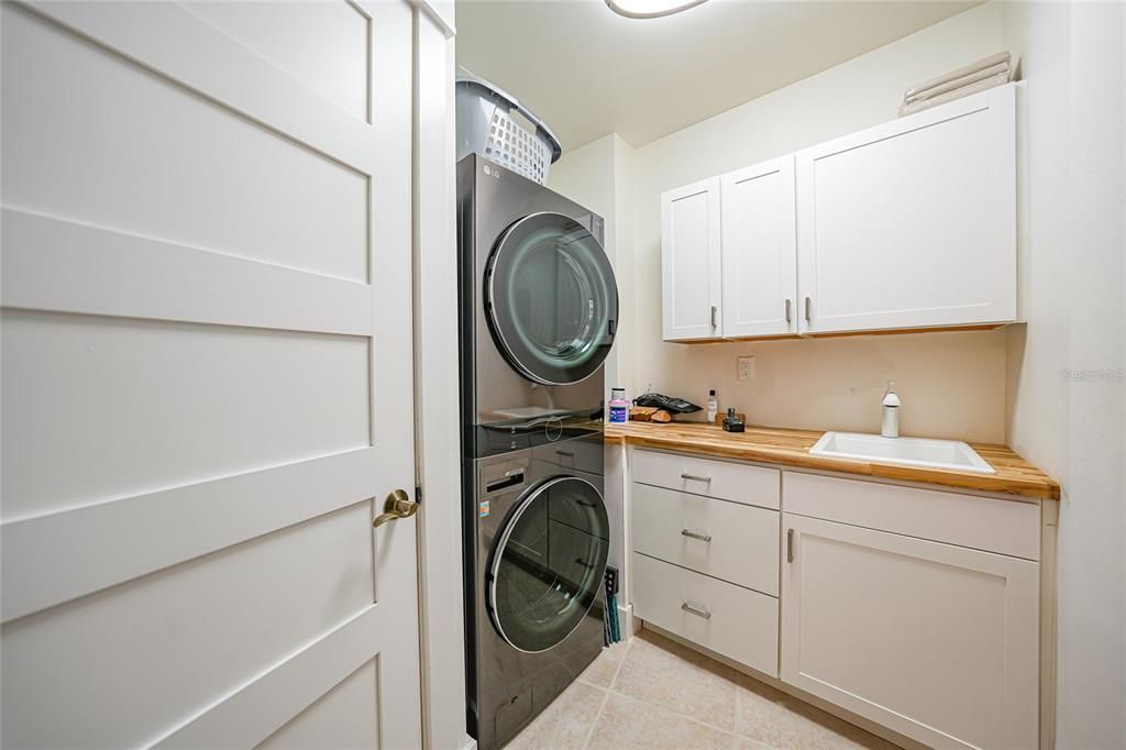 Large laundry room with newer stackable washer and dryer. Sink and lots of storage. Door to left has the HW Heater and more storage.