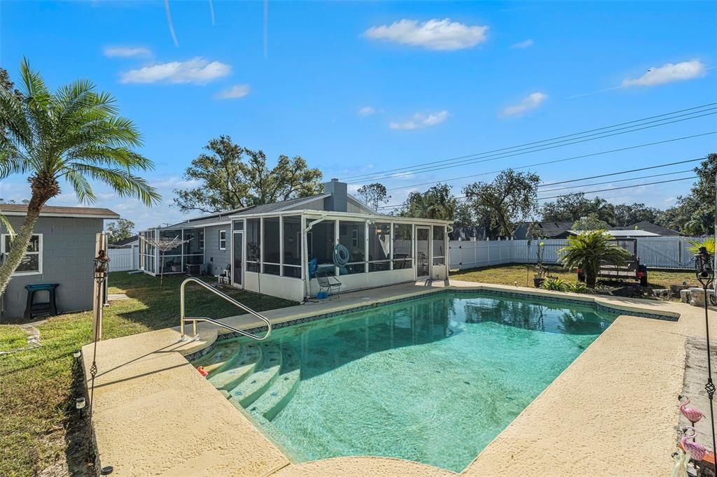 Large in ground pool overlooking outdoor shower and screened lanai