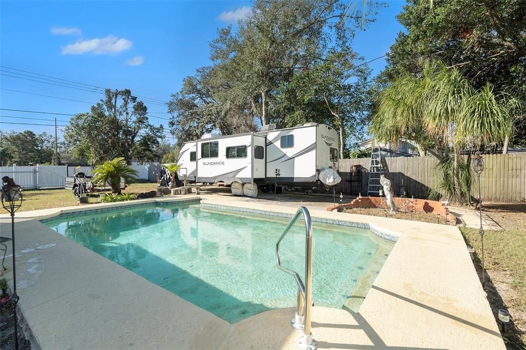 Large in ground pool overlooking RV concrete parking pad with RV outlet