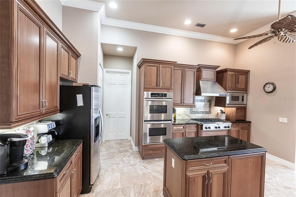 The gourmet kitchen is a chef’s dream, featuring granite countertops, custom wood cabinetry, a center island, breakfast bar, and premium stainless steel appliances, including a 6-burner gas range with hood and built-in double ovens.