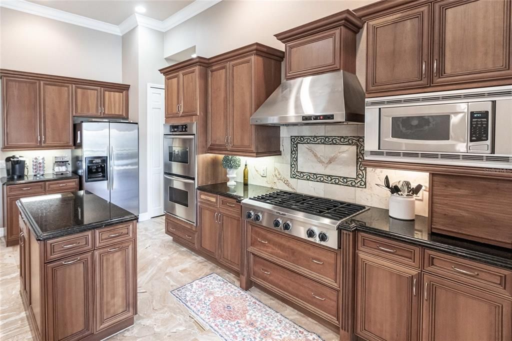 The gourmet kitchen is a chef’s dream, featuring granite countertops, custom wood cabinetry, a center island, breakfast bar, and premium stainless steel appliances, including a 6-burner gas range with hood and built-in double ovens.