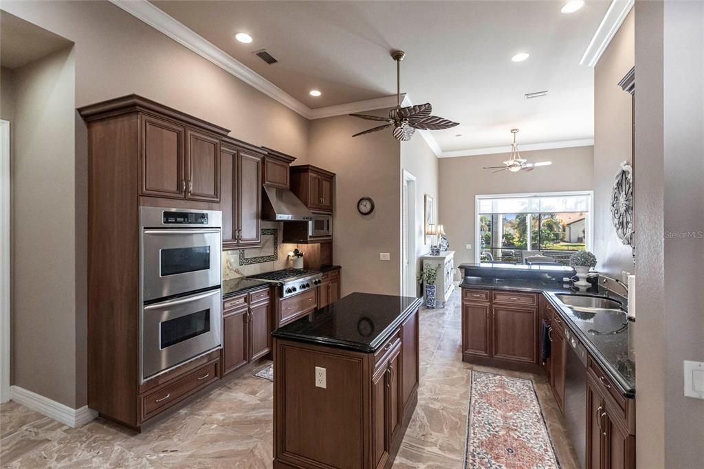 The gourmet kitchen is a chef’s dream, featuring granite countertops, custom wood cabinetry, a center island, breakfast bar, and premium stainless steel appliances, including a 6-burner gas range with hood and built-in double ovens.