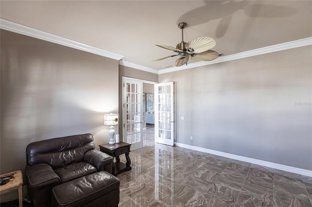 Front-facing office/den with French doors, ceiling fan, and multiple windows.