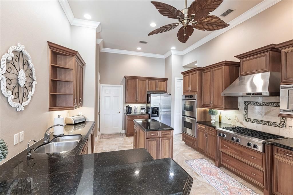 The gourmet kitchen is a chef’s dream, featuring granite countertops, custom wood cabinetry, a center island, breakfast bar, and premium stainless steel appliances, including a 6-burner gas range with hood and built-in double ovens.