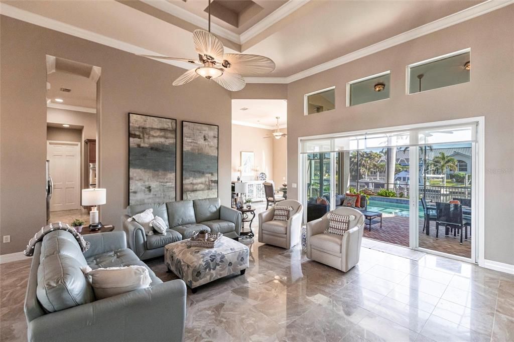 Exquisite living room is highlighted by 10' coffered ceilings, elegant columns, crown molding, and large windows with pool and canal views.