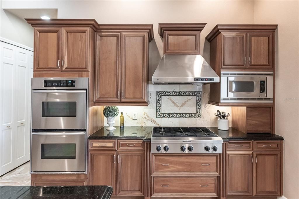 The gourmet kitchen is a chef’s dream, featuring granite countertops, custom wood cabinetry, a center island, breakfast bar, and premium stainless steel appliances, including a 6-burner gas range with hood and built-in double ovens.