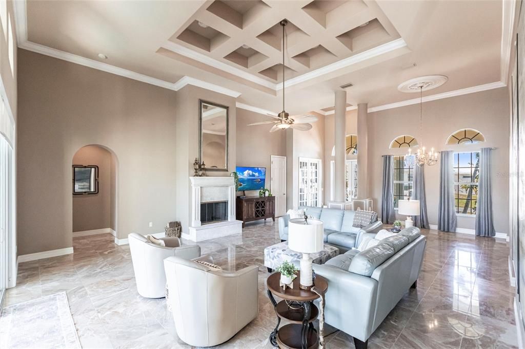 Exquisite living room is highlighted by 10' coffered ceilings, elegant columns, crown molding, and large windows with pool and canal views.