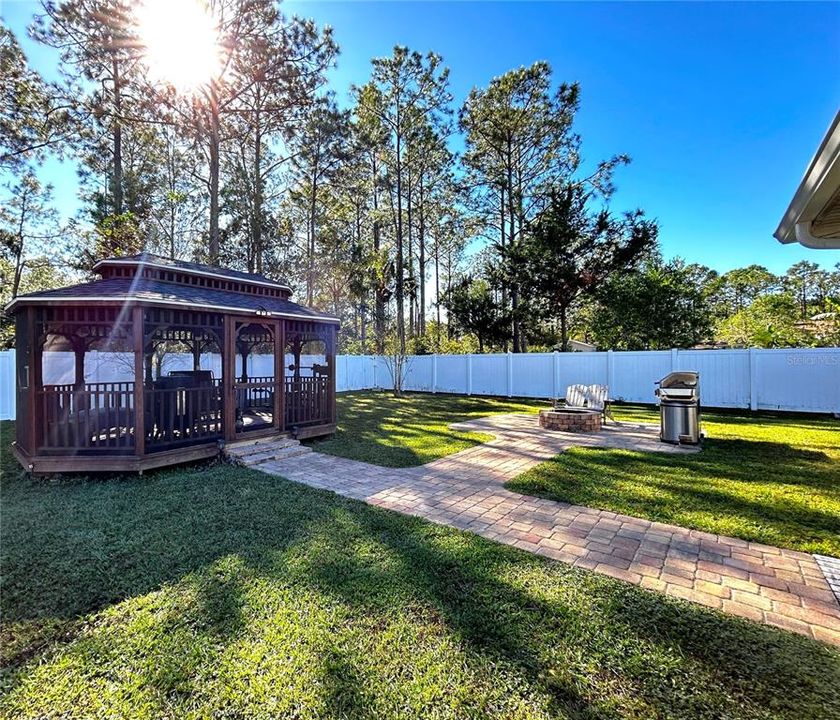 A beautifully paved walkway leads you to a charming outdoor space featuring an enchanting gazebo, cozy fireplace and BBQ grill