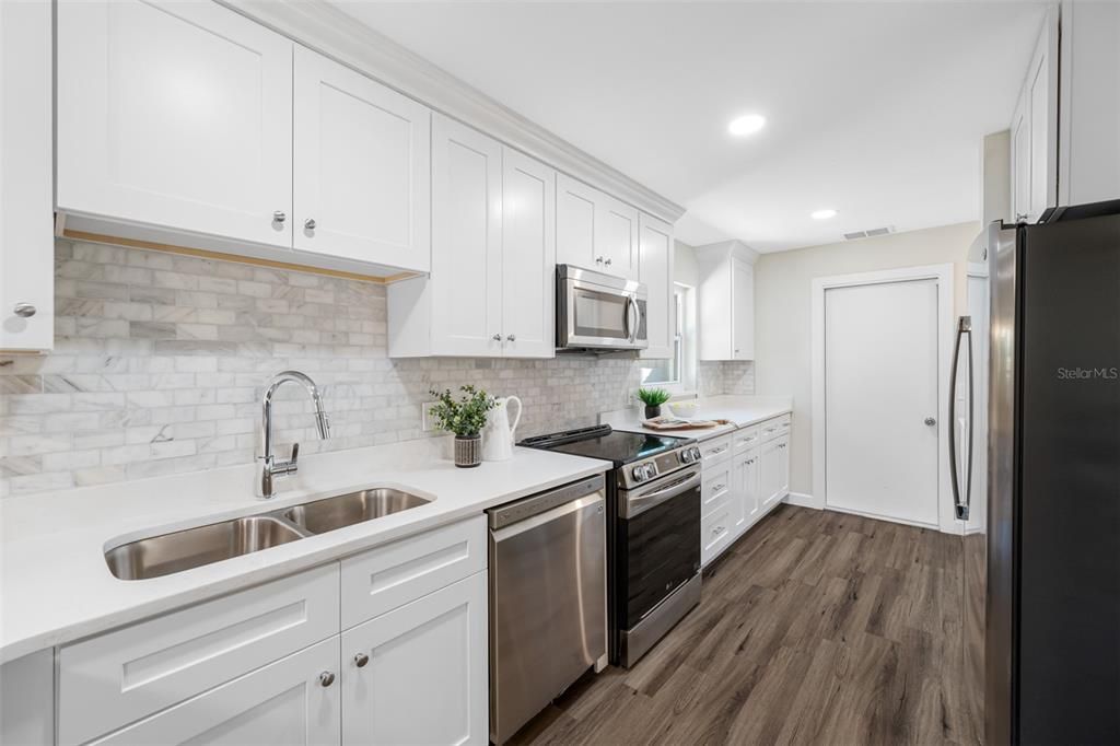 Renovations include custom wood cabinets in white finish with quartz countertops and stainless steel hardware, new appliances, double stainless steel sink, faucet, marble tile backsplash