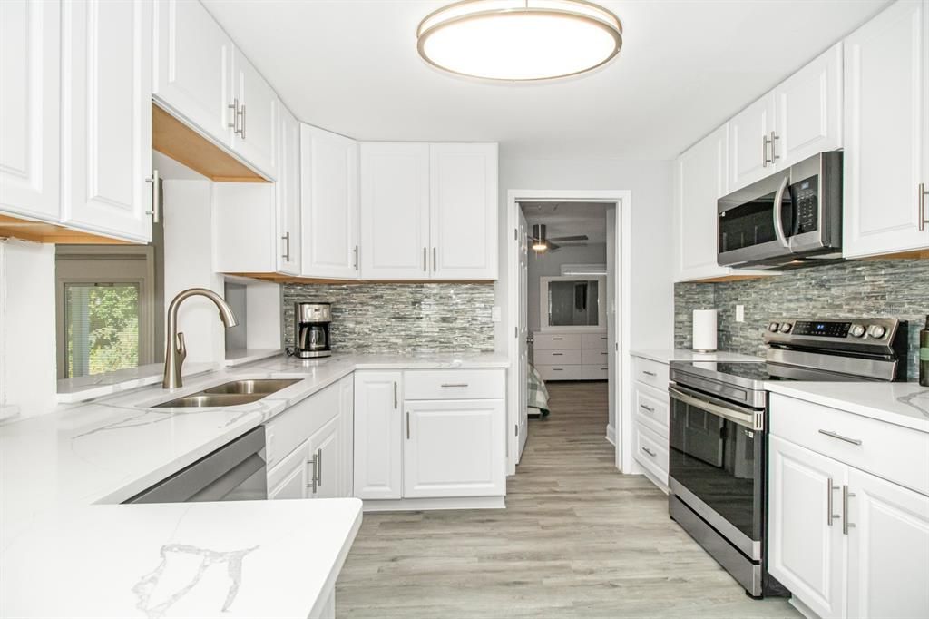 The kitchen is a chef's dream with luxurious QUARTZ countertops, a COFFEE BAR AREA with a PREMIUM WINE/BEVERAGE COOLER, STAINLESS STEEL SAMSUNG APPLIANCES, new cabinets with a lazy susan corner cabinet, LED lighting, new sink and fixture, new garbage disposal, and custom tiled backsplash.