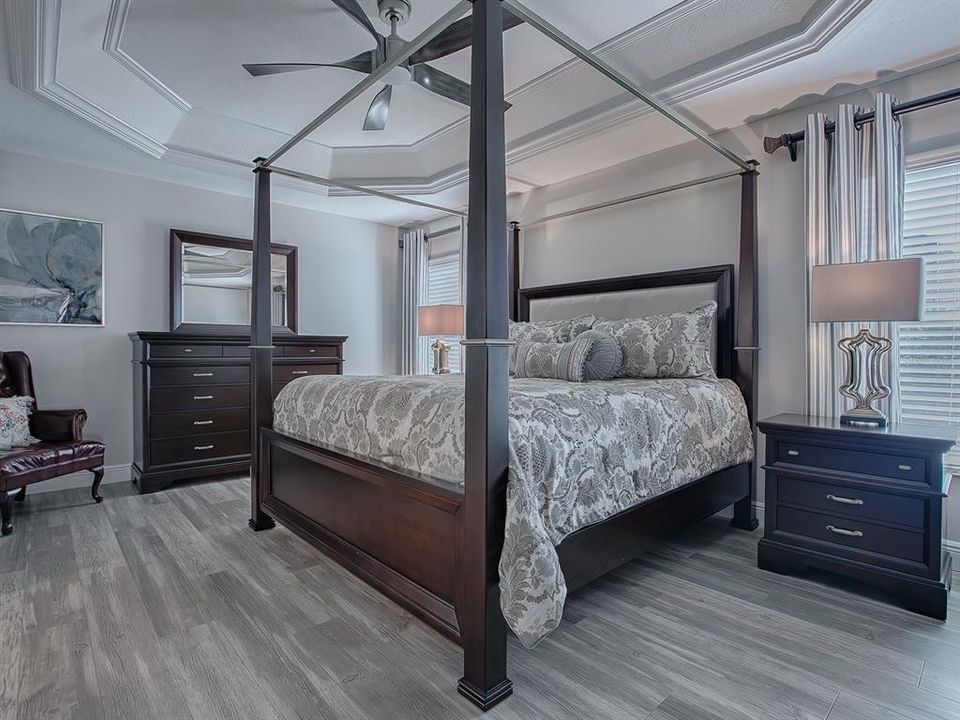 PRIMARY BEDROOM WITH LUXURY VINYL PLANK FLOORING, AND CROWN TRIMMED TRAY WITH CUSTOM CEILING FAN.