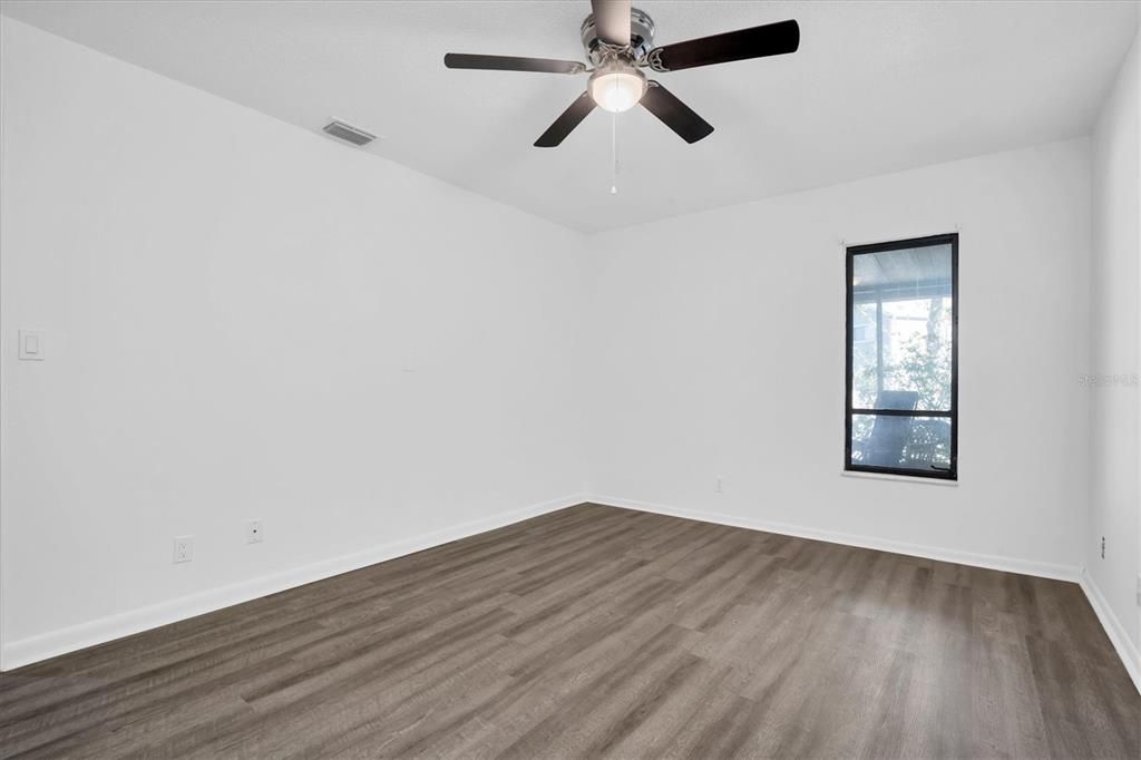 Primary bedroom. Has window to the back porch and beyond. Good view of the luxury vinyl flooring. New ceiling fan!