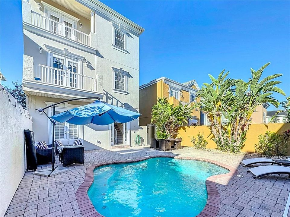 A spacious pool deck, made of brick pavers, extends around the water, offering plenty of room for relaxation.