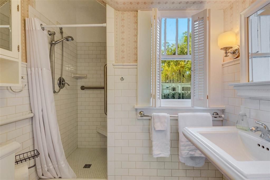 White subway, 1" mosaic hex on the floor and shower, tile chair rail, sconces, and pedestal sink. Is that Laura Ashley wallpaper? This bathroom could teach a class on historic preservation