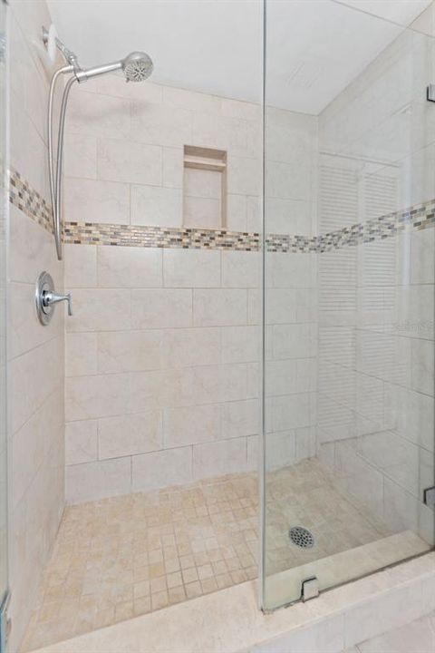 Beautifully tiled glass enclosed shower in the primary suite bathroom.