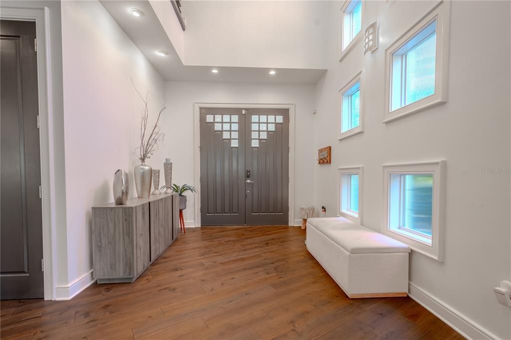 The entry foyer is massive and inviting, setting the tone for the home with neutral tones, high ceilings, wood floors, statement front doors, and a wall of windows that mimic a gallery wall.