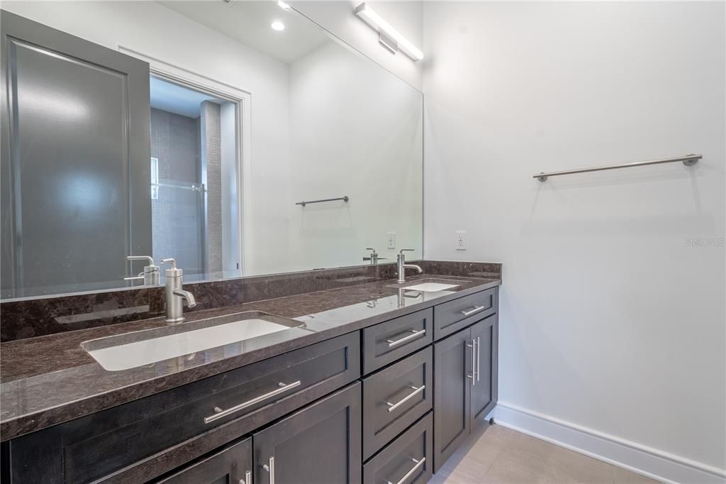 The 2nd bathroom features a mirrored dual sink, wood vanity with storage, granite counter top and modern light fixtures.