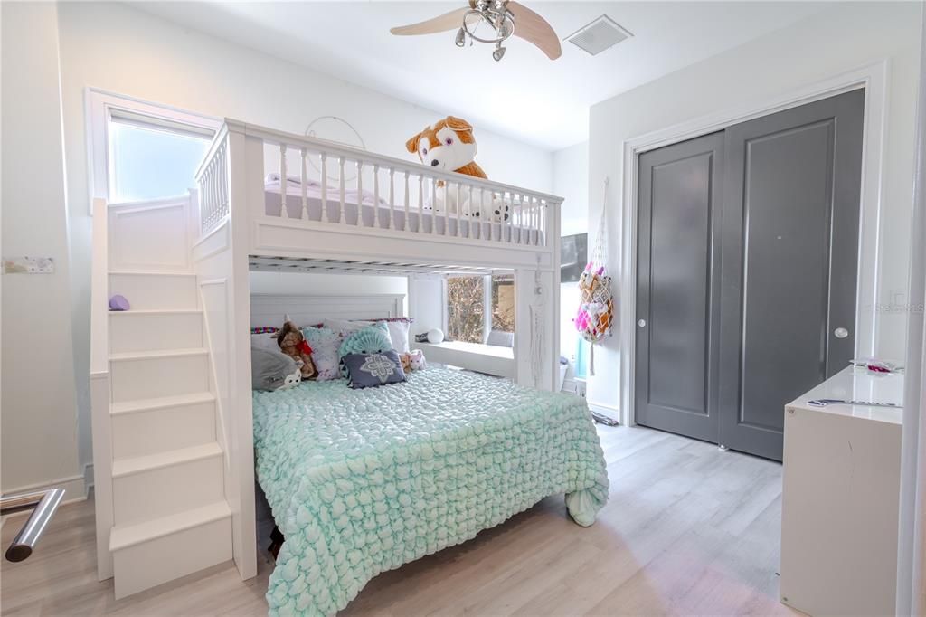 The 5th bedroom features wood laminate flooring, a built in closet with dark wood paneled sliding closet doors, a ceiling fan and ensuite bath.