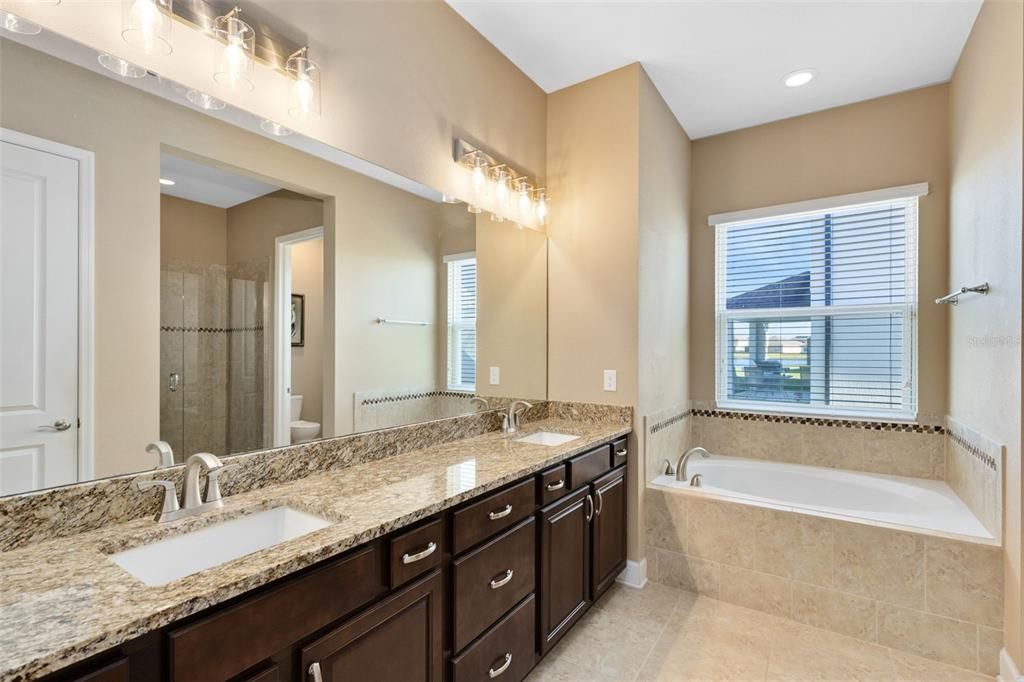 The spa-like primary bath showcases a dual granite-topped vanity, a luxurious soaking tub, and a frameless glass-enclosed shower.