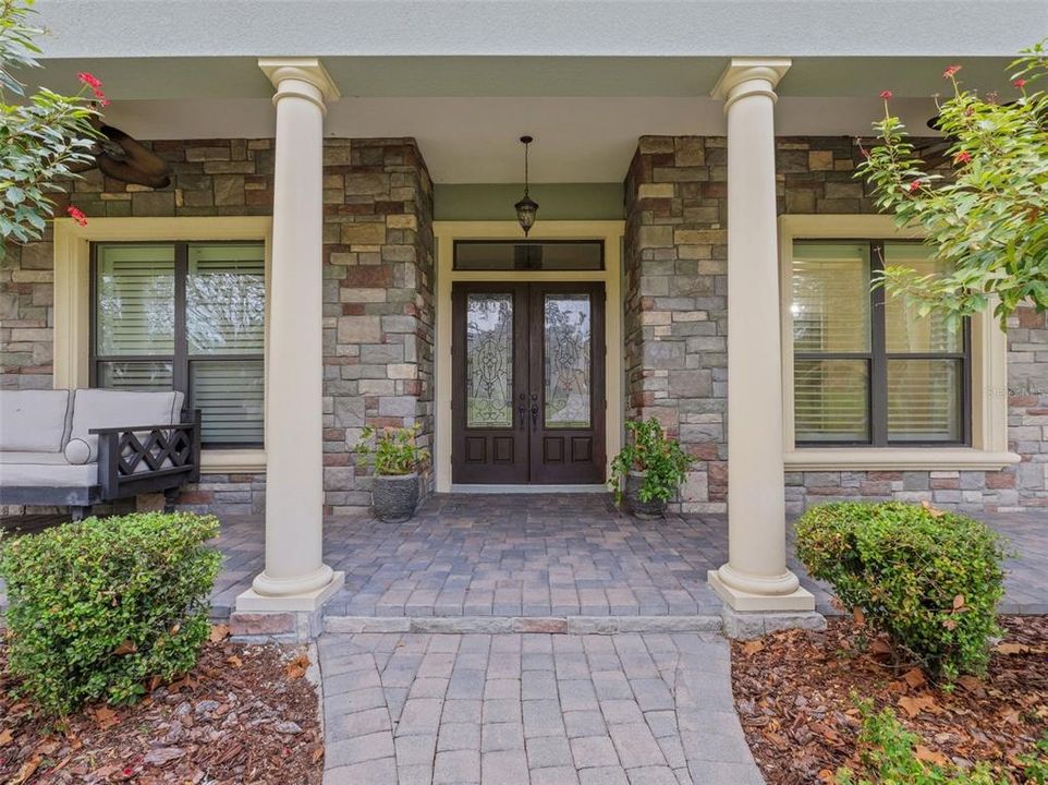 Stunning double custom front doors. The front walk-way & inviting front porch feature stunning pavers, custom stone... along with it being beautifully landscape.