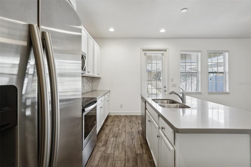 large kitchen that includes an oversized island, Corian Countertops, White Cabinets, Stainless Steel Appliances and Tile Backsplash!