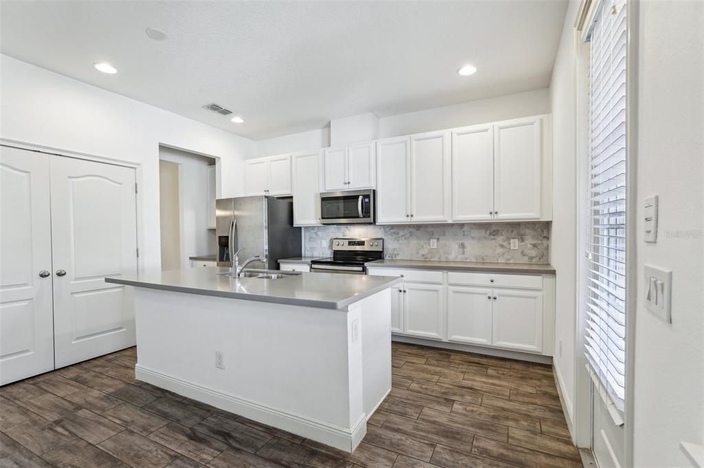 large kitchen that includes an oversized island, Corian Countertops, White Cabinets, Stainless Steel Appliances and Tile Backsplash!