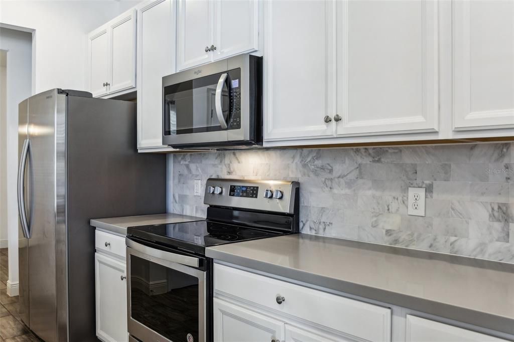 large kitchen that includes an oversized island, Corian Countertops, White Cabinets, Stainless Steel Appliances and Tile Backsplash!