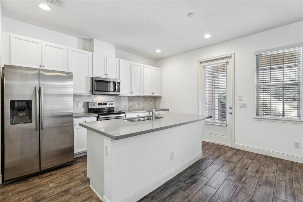 large kitchen that includes an oversized island, Corian Countertops, White Cabinets, Stainless Steel Appliances and Tile Backsplash!