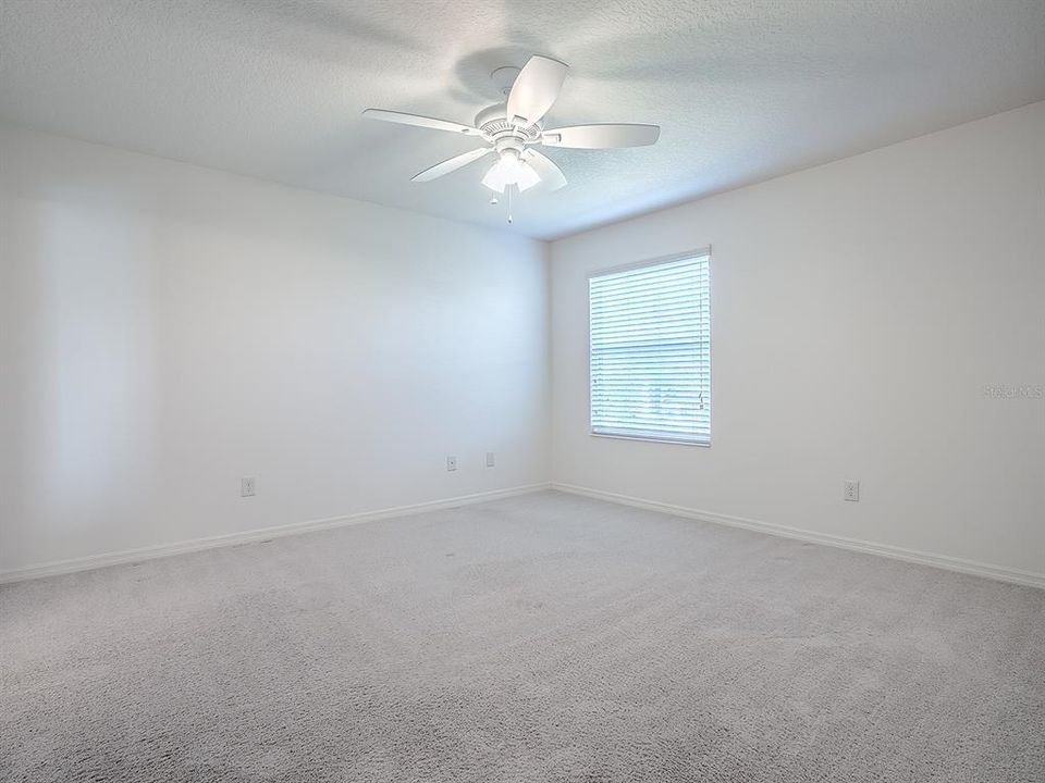 PRIMARY BEDROOM WITH CARPET AND CEILING FAN.