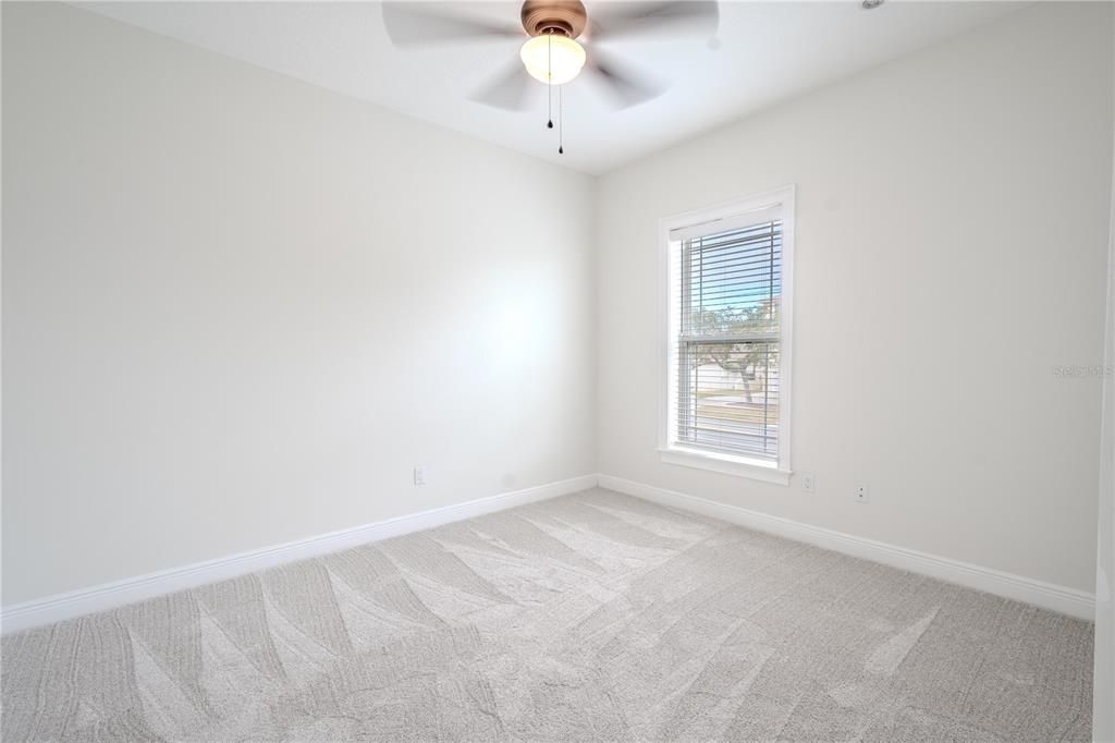 The 4th bedroom features a new, neutral-tone carpet and walls, a built-in closet, a ceiling fan, and window blinds.