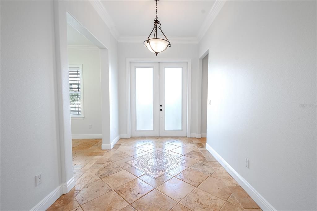 Double glass pane front doors open to the foyer with an artistic travertine tile design.