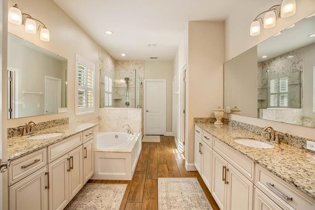 Primary bathroom w/ dual sinks and Turkish marble tile surrounding the tub and shower area. walk-in closet with custom shelving and second closet.