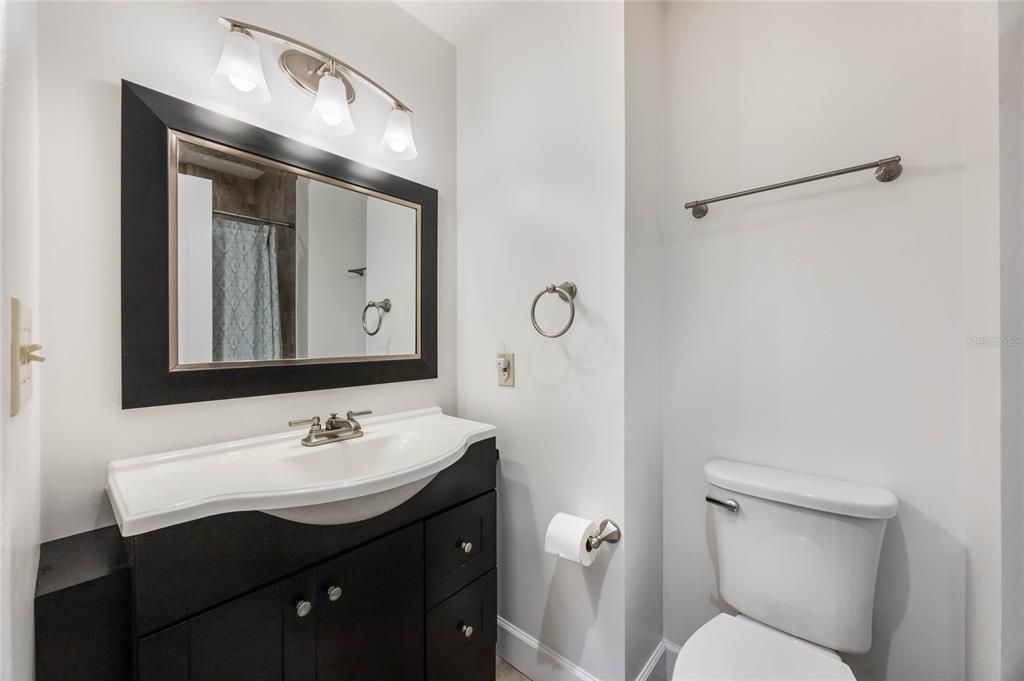 This photo shows the guest bath on the 2nd level with a dark wood vanite with white stone counters and light grey neutral wall colors.