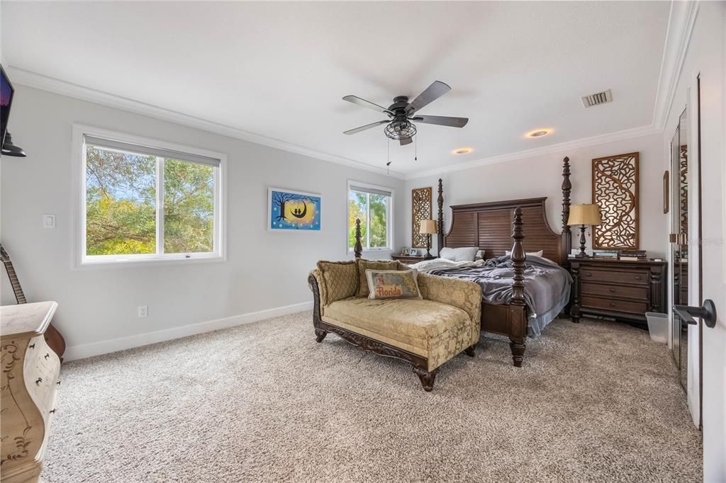 View into the primary bedroom with carpet throughout. To the left of the large bed are two brand new windows, above the bed is a ceiling fan and to the right are the doors to the closets.