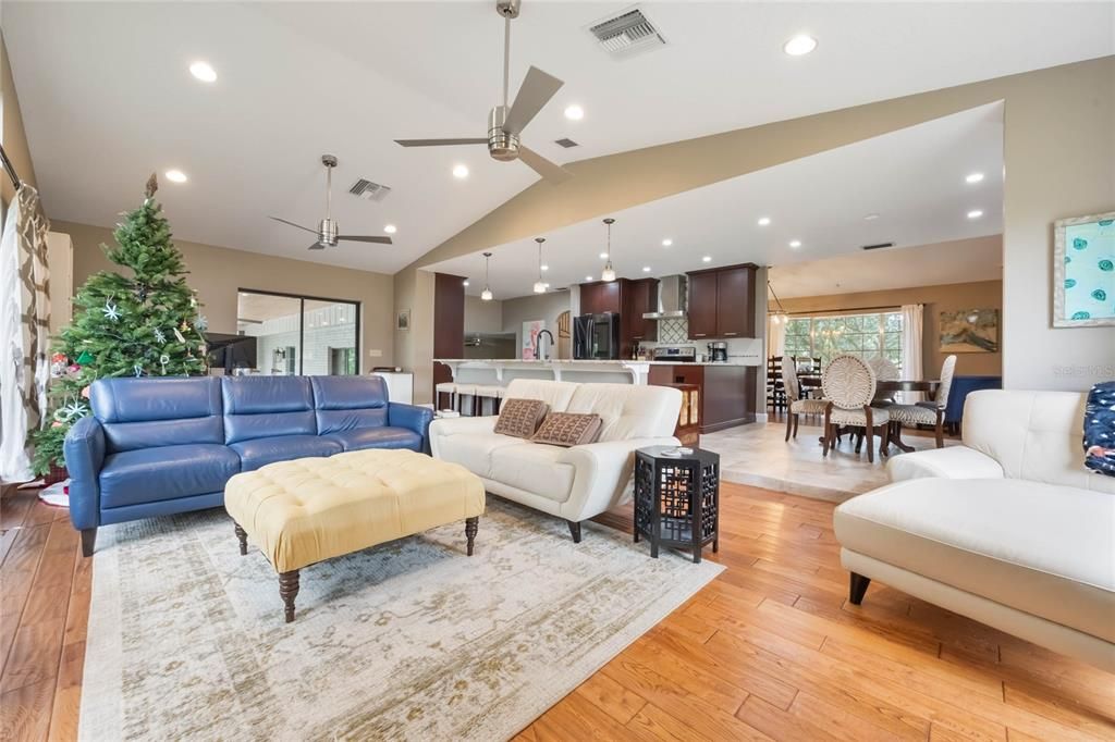 This photo shows the family room looking toward the kitchen with a large arm chair to the right, a small breakfast table just behind. A sofa that matches the arm chair is in the center with the kitchen island behind it. To the left of the image is a blue leather sofa with the christmas tree behind.