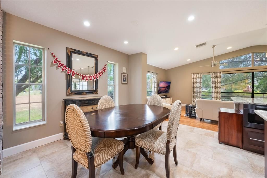 This photo is an image of the breakfast nook that features a small oval table with 4 chairs. Behind that is a large hanging mirror flanked by a window on each side.