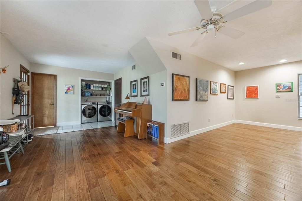 This photo shows an l-shaped bonus room located on the lower level of the home. To the right is an open area that can be used as another dining area or sitting room, and to the left is another open area that has the laundry close and door to the full bath. On the left side of the image is the door that leads to the backyard.