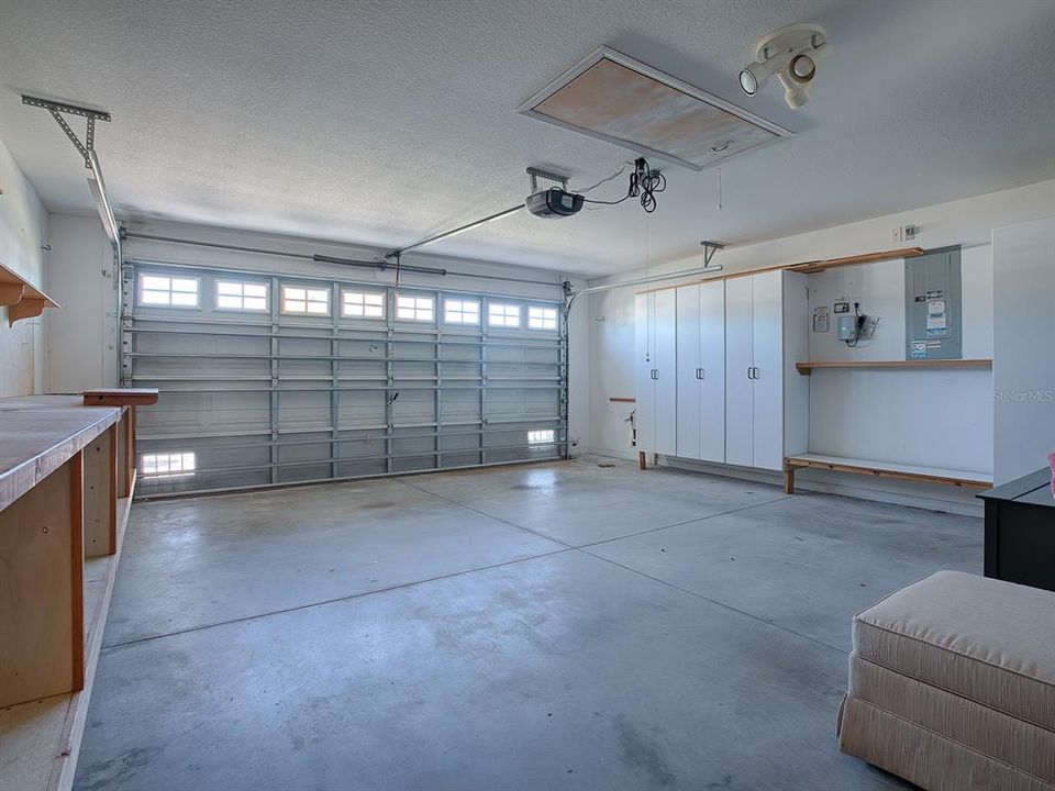 SPACIOUS TWO-CAR GARAGE HAS CABINETS AND SHELVING ALONG WITH A WORKSHOP AREA