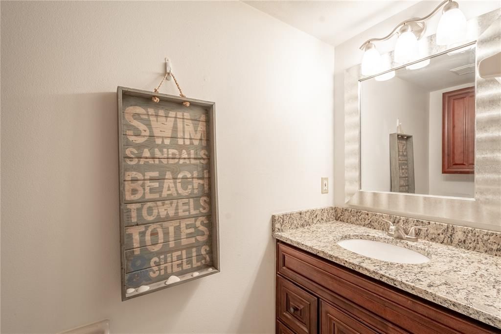 The downstairs powder room features a mirrored wood vanity with storage, downlight fixture and granite counter top.