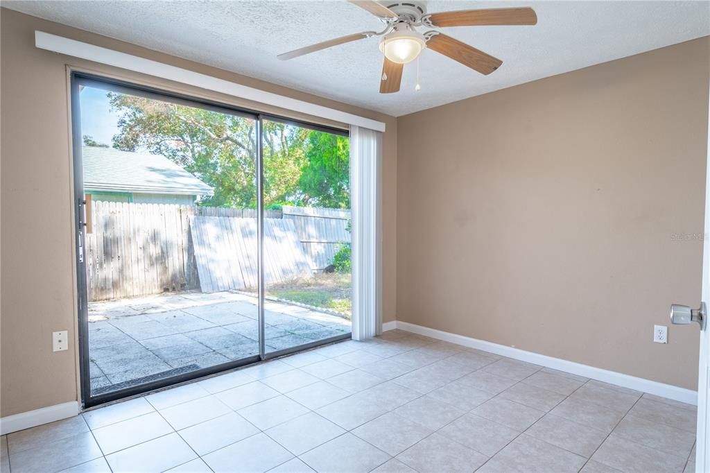 The 2nd bedroom features neutral tones, ceramic tile flooring, a built-in closet, ceiling fan with light kit and sliding glass doors to the back patio.