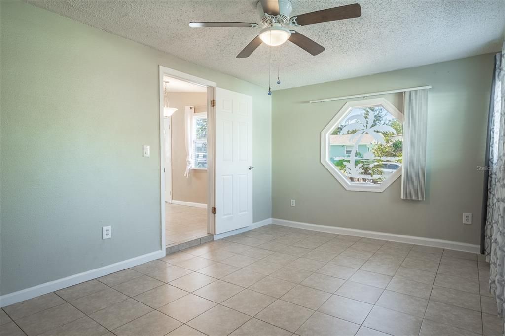 The Primary bedroom features neutral tones, ceramic tile flooring, ceiling fan with light kit and an etched octagon picture window