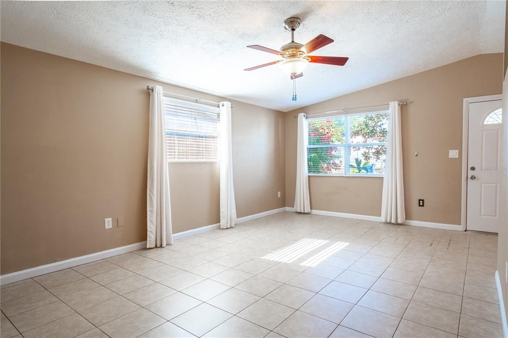 The living room has a neutral color palette, vaulted ceiling, ceiling fan with light kit and ceramic tile floor.