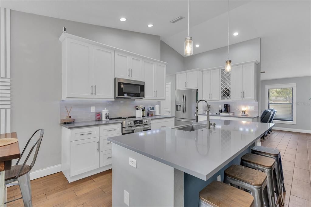 Large Kitchen Island with farm house sink. Stone quartz countertops, breakfast bar, dry bar, custom cabinets, under cabinet lights, newer kitchen appliances.