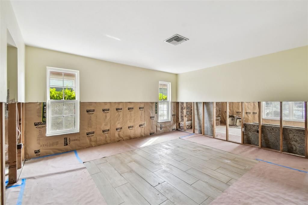 Primary bedroom with the family room seen through the half wall exposing the brick fireplace.