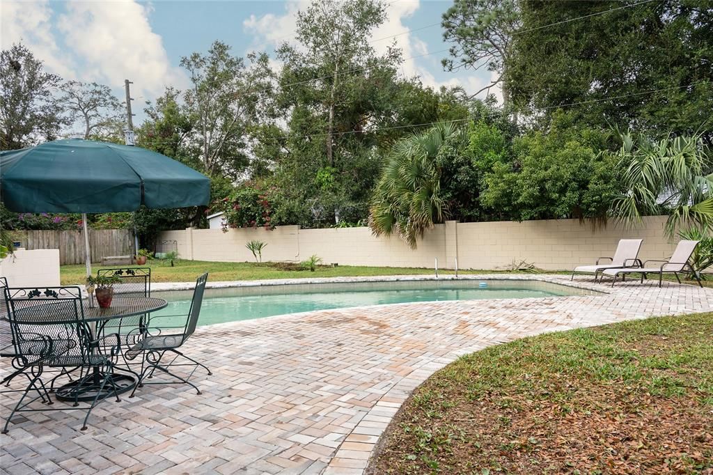 Backyard with pavers surrounding pool. Back concrete wall freshly painted