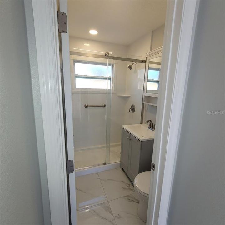 The bathroom shower, with a glass door, new vanity, toilet, and flooring make this bathroom special.